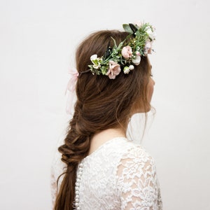 May include: A woman with long brown hair wearing a white lace dress and a floral crown with pink and white flowers.