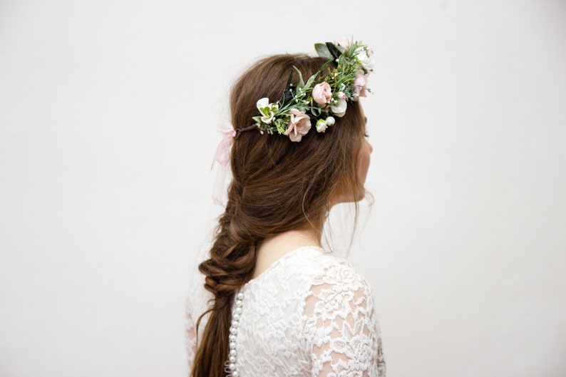 May include: A woman with long brown hair wearing a white lace dress and a floral crown with pink and white flowers.