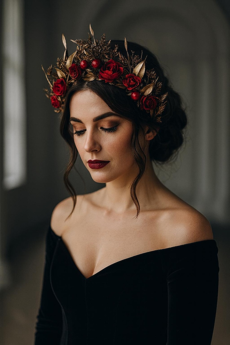 May include: A dark-haired person wearing a black off-the-shoulder dress and a floral crown. The crown features red roses, gold leaves, and berries. The person has dark lipstick and closed eyes.