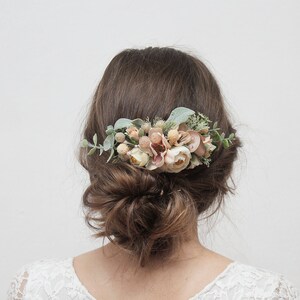 May include: A floral hair comb with blush pink and white flowers and greenery. The comb is worn in a woman's hair.
