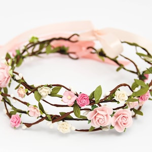 May include: A delicate floral crown made of brown twigs, pink and white fabric flowers, and green leaves.