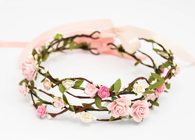 May include: A delicate floral crown made of brown twigs, pink and white fabric flowers, and green leaves.