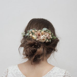 May include: A floral hair comb with blush pink and peach flowers and greenery. The comb is worn in a woman's hair.
