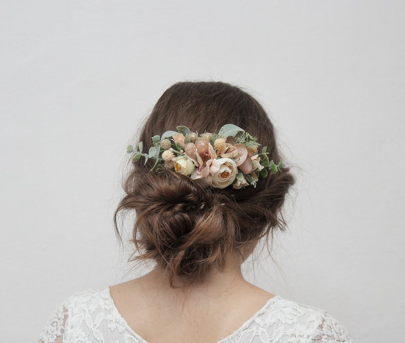 May include: A floral hair comb with blush pink and peach flowers and greenery. The comb is worn in a woman's hair.