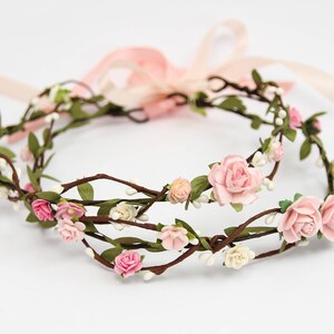 May include: A double-layered floral crown with pink and white flowers on brown branches. The crown is made of artificial flowers and is tied with a pink ribbon.