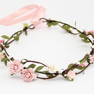 May include: A pink floral crown with small pink roses and white flowers on a brown vine base. The crown is tied with a pink ribbon.