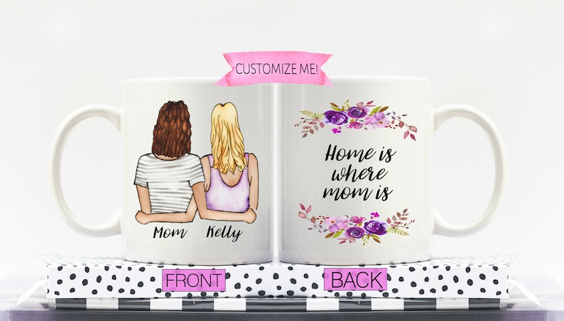 Pu&ograve; includere: Una tazza in ceramica bianca con un design floreale e il testo "Home is where mom is" sul retro. La parte anteriore della tazza presenta un'illustrazione di due donne con i nomi "Mom" e "Kelly" scritti sotto.
