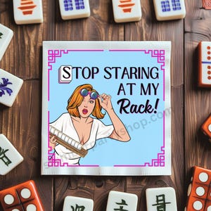 Op de afbeelding: Een vierkante, lichtblauwe Mahjong-servet met een pop-art-stijl illustratie van een vrouw die een zonnebril en een Mahjong-rek vasthoudt. De tekst op de servet luidt "STOP STARING AT MY Rack!" omgeven door een roze rand. Mahjong-tegels zijn verspreid.