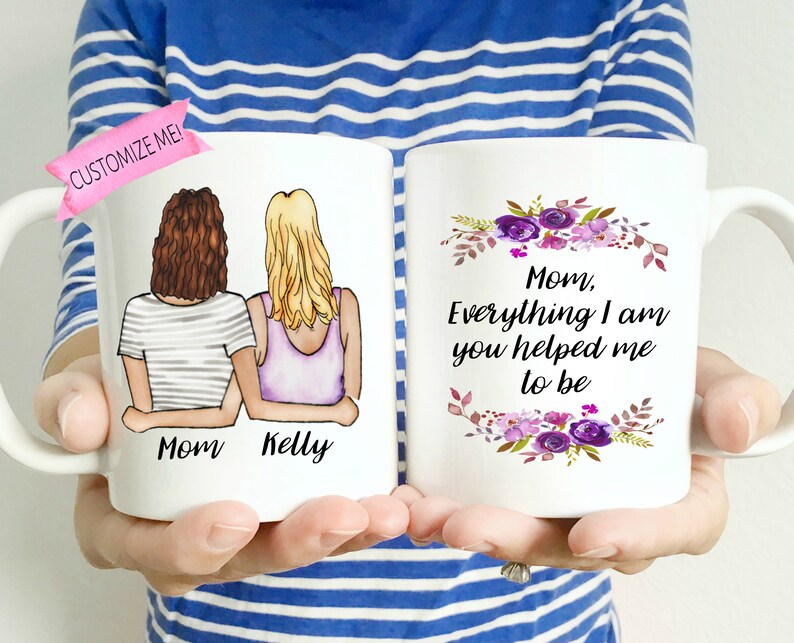 Pu&ograve; includere: Due tazze in ceramica bianca con un design floreale e il testo "Mamma, tutto ci&ograve; che sono, mi hai aiutato ad essere". Una tazza presenta un'illustrazione disegnata a mano di due donne con il testo "Mamma Kelly".