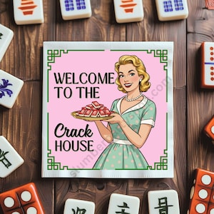 May include: A square, pink and green printed Mahjong tile holder with the text "WELCOME TO THE CRACK HOUSE" and a retro illustration of a woman holding a tray of tiles. Mahjong tiles and dice surround the holder.