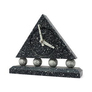 May include: A black and white speckled triangular clock with a round clock face. The clock hands are white. The clock sits on three spherical supports above a rectangular base.
