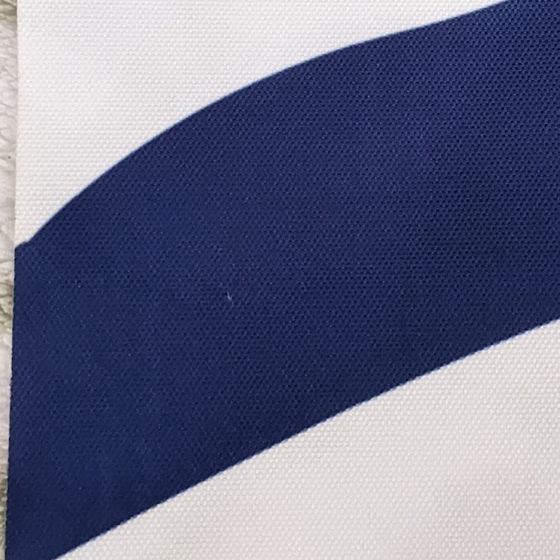 May include: Close-up of a white and navy blue striped fabric. The fabric has a textured, woven appearance.