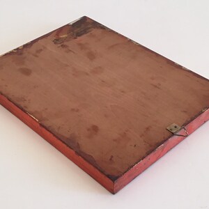 May include: A rectangular wooden plaque with a red painted frame and a brown interior. The plaque has a metal hanger attached to the back. The edges of the frame show signs of wear and tear.