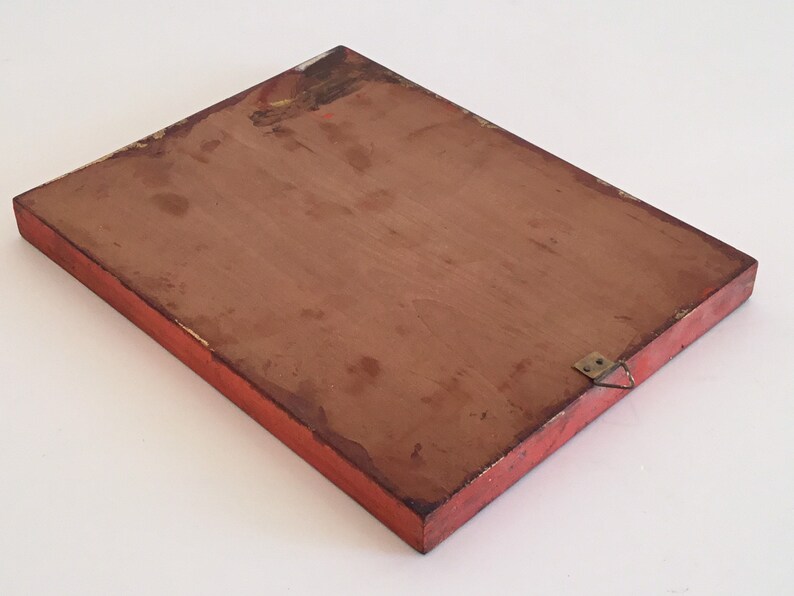 May include: A rectangular wooden plaque with a red painted frame and a brown interior. The plaque has a metal hanger attached to the back. The edges of the frame show signs of wear and tear.