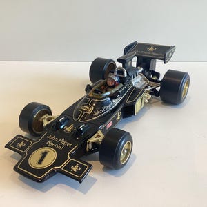 May include: A black and gold John Player Special race car model. The car features the number 1, gold wheels, and the John Player Special logo. The model has a driver figure and a rear spoiler.