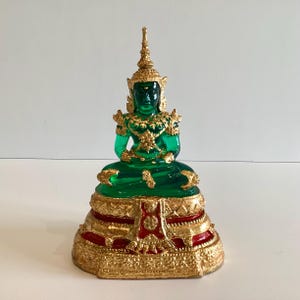 May include: A seated Buddha statue with a vibrant green body and intricate gold detailing. The statue features a gold crown and ornate embellishments. The base is gold with red accents, creating a striking contrast. The statue is a representation of Buddhist art.