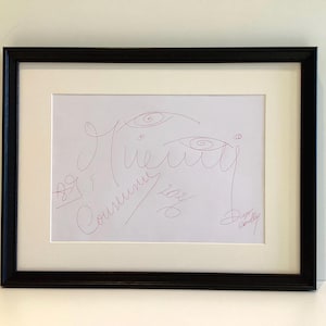 May include: Framed artwork with a minimalist red ink line drawing on white paper. The drawing depicts abstract facial features and cursive text, set in a black frame with a white mount. Signed and dated.