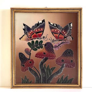 Può includere: Opera d'arte incorniciata con due farfalle con ali rosse, arancioni e nere appollaiate su funghi stilizzati. L'opera ha uno sfondo marrone ed è incorniciata in una cornice dorata.