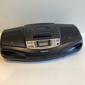 May include: Black Panasonic boombox with a cassette player, speakers, and a digital tuner. The boombox has a silver control panel with a digital display and buttons. The Panasonic logo is visible on the front.