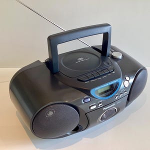 May include: A black Panasonic portable CD player and radio with a handle, aerial, and speakers. The CD player is on top, with buttons and a digital display. The radio has a blue accent around the display and the brand name is visible.
