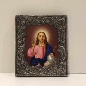 May include: A religious icon featuring a depiction of Jesus Christ. The image shows Jesus with long brown hair, wearing a pink robe and blue cloak, holding a globe and a star. The image is set within an ornate silver frame.