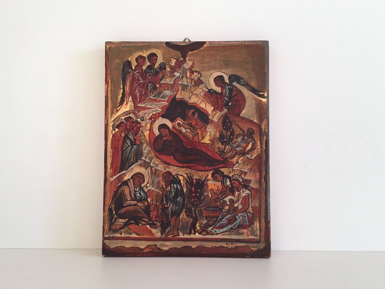 May include: A religious icon depicting a nativity scene with figures in red, brown, and gold tones. Angels and other figures surround the central figures. The icon is mounted on a wooden panel.