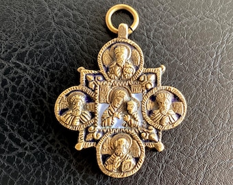 Puede incluir: Colgante dorado con diseño de cruz. El colgante presenta figuras religiosas en marcos circulares y una imagen central de una madre y un niño. La cruz tiene un borde de esmalte azul y un pequeño lazo en la parte superior.