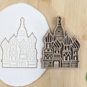 Pode incluir: Um cortador de biscoitos de plástico marrom em forma da Catedral de São Basílio em Moscou, Rússia. O cortador é mostrado ao lado de uma massa branca com o contorno da catedral cortado nela. O cortador é etiquetado como "Food Grade".