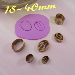 Könnte beinhalten: Ein Set mit 7 goldfarbenen Ausstechern in verschiedenen Größen und Formen, darunter Kreise und Kaffebohnenformen. Die Ausstecher befinden sich auf einer rosa Oberfläche. Der Text "15-40mm" ist oben im Bild in Gelb geschrieben.