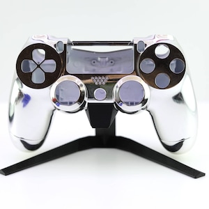 Könnte beinhalten: Ein silberner PlayStation 4-Controller mit einem schwarzen Ständer. Der Controller hat eine silberne Frontplatte und schwarze Tasten.