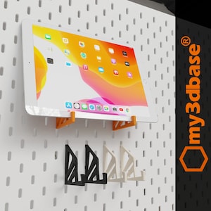 Op de afbeelding: Oranje, zwarte en witte wandbevestigingen voor tablet en telefoon. De houders zijn ontworpen om te passen op prikborden. De tekst "my3dbase®" staat in de hoek van de afbeelding.