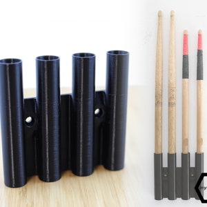 Pode incluir: Um suporte de parede de plástico preto com quatro ranhuras para guardar baquetas. O suporte está montado numa superfície de madeira. As baquetas não estão incluídas.