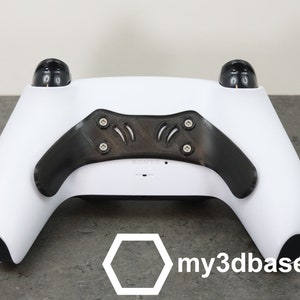 Könnte beinhalten: Ein weißer PlayStation 5 DualSense-Controller mit schwarzen Rückseiten-Paddeln und einem schwarzen "my3dbase"-Logo auf der Rückseite.