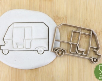 May include: A brown plastic cookie cutter shaped like a tuk tuk, a three-wheeled vehicle common in Southeast Asia. The cookie cutter is on a wooden surface.