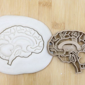 Puede incluir: Un cortador de galletas de plástico marrón con forma de cerebro humano. El cortador está sobre una superficie de madera y tiene una etiqueta "Food Grade".