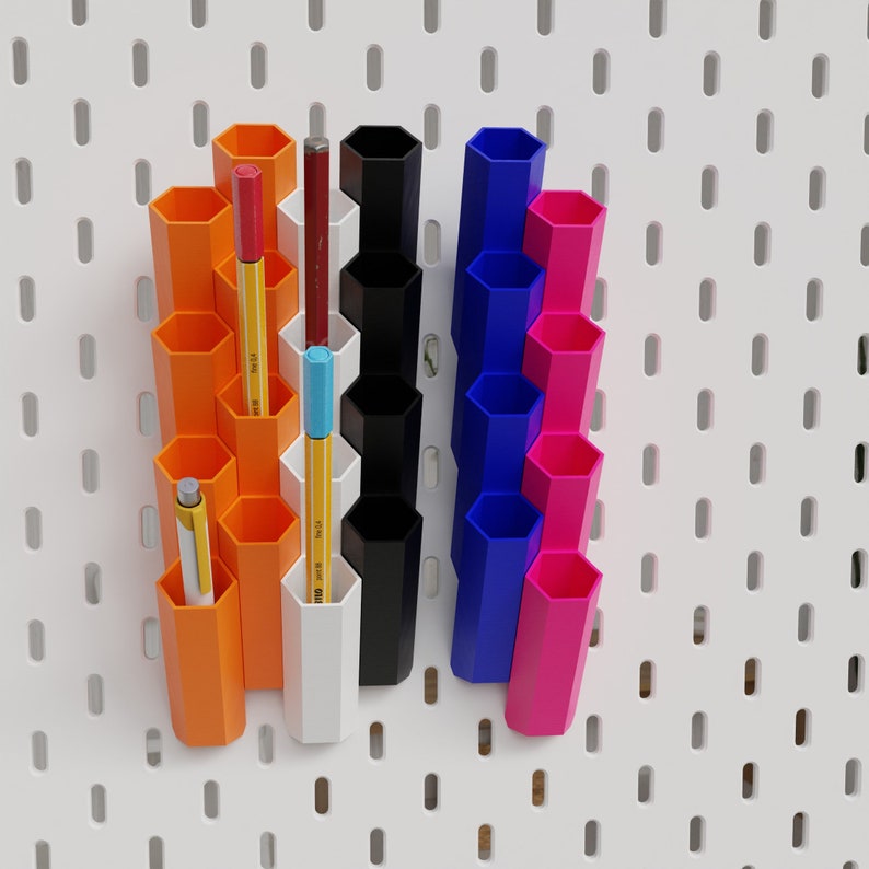 Puede incluir: Un organizador de pared de tablero perforado con m&uacute;ltiples compartimentos en naranja, blanco, azul y rosa. Los compartimentos contienen bol&iacute;grafos, l&aacute;pices y marcadores.