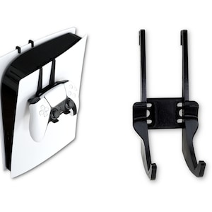 Könnte beinhalten: Eine schwarze Wandhalterung für eine PlayStation 5 Konsole und einen Controller. Die Halterung hat zwei Haken zum Aufhängen des Controllers und ein Regal für die Konsole.