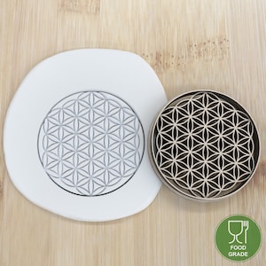 Könnte beinhalten: Eine weiße Silikonform und ein Holz-Ausstecher, beide mit einem kreisförmigen Design eines Lebensblumenmusters. Der Ausstecher ist lebensmittelecht.