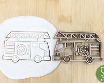 May include: A metal cookie cutter in the shape of a fire truck with a ladder on top. The cutter is food grade and is shown next to a piece of white fondant.
