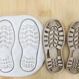 Könnte beinhalten: Zwei lebensmittelechte Ausstecher aus Kunststoff in Form einer Schuhsohle. Die Ausstecher liegen auf einer Holzoberfläche.