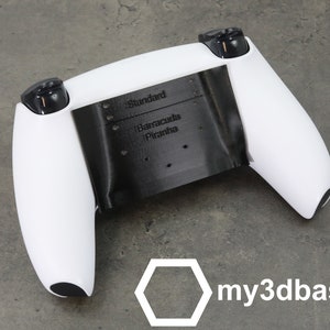 Könnte beinhalten: Ein weißer PlayStation 5 DualSense-Controller mit einer schwarzen, 3D-gedruckten Rückplatte. Die Rückplatte trägt den Text "Standard", "Barracuda" und "Piranha". Der Text "my3dbase" ist in der unteren rechten Ecke des Bildes gedruckt.