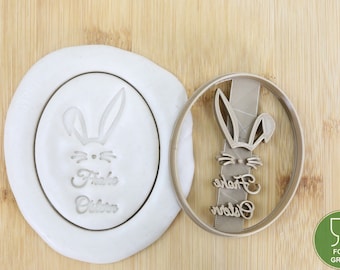 May include: A food-grade cookie cutter in the shape of a bunny rabbit with the text "Frohe Ostern" in a cursive font. The cutter is shown on a white surface with a sample impression of the cutter in the dough.