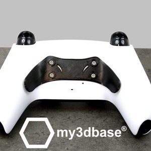 Könnte beinhalten: Weißer Gaming-Controller mit schwarzen Akzenten und einer Carbonfaser-Textur auf der Rückseite. Der Controller hat ein Logo mit der Aufschrift "my3dbase" auf der Unterseite.
