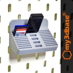 Könnte beinhalten: Grauer, wandmontierter Aufbewahrungsorganisator aus Kunststoff mit Steckplätzen für Speicherkarten und einen USB-Stick. Der Organizer hat einen Steckplatz für eine SD-Karte mit dem sichtbaren Text "Sandisk 32 GB". Der Organizer ist mit "my3dbase" und einem eingetragenen Warenzeichen gekennzeichnet.