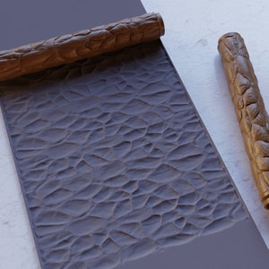 Könnte beinhalten: Zwei braune Gummifahrwerke mit einer strukturierten Oberfläche, die verwendet werden, um ein steinartiges Muster auf einer Oberfläche zu erzeugen. Die Walzen befinden sich auf einem grauen Hintergrund.