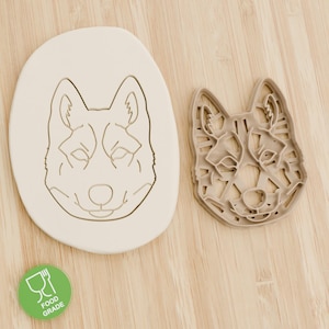 Könnte beinhalten: Ein Hund-förmiger Ausstecher und sein Abdruck auf einer hellen Oberfläche. Der Ausstecher ist eine detaillierte Umrisszeichnung eines Hundegesichts, und der Abdruck zeigt das gleiche Design. Ein grüner Aufkleber in Lebensmittelqualität befindet sich in der linken unteren Ecke.