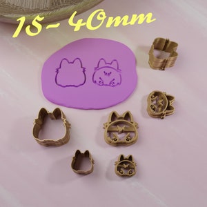 Puede incluir: Un juego de seis cortadores de galletas de color dorado en forma de gato. Los cortadores son de diferentes tamaños, siendo el más grande de 40 mm. Los cortadores están sobre una superficie rosa.