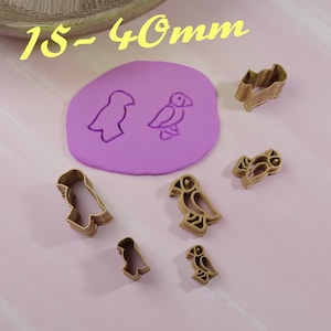 May include: A set of six gold-colored cookie cutters shaped like puffins, ranging in size from 1.5 to 4 cm. The cutters are arranged on a pink surface, with a purple silicone mold in the background.