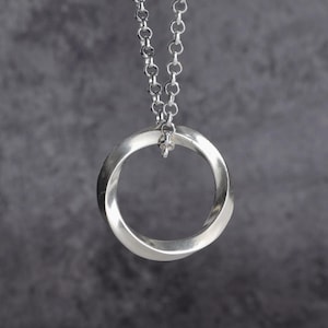 May include: A silver-colored pendant necklace featuring a Mobius strip design. The pendant is a continuous loop, suspended from a delicate chain. The necklace is displayed against a gray background, highlighting the polished metal.