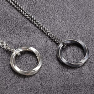 May include: Two silver-toned pendant necklaces. Each necklace features a circular pendant with a twisted design, suspended from a delicate chain. The pendants have a polished finish, and the chains are also silver.